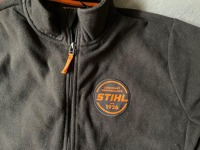 Dettaglio giacca in pile Stihl con patch logo e cursore zip arancione
